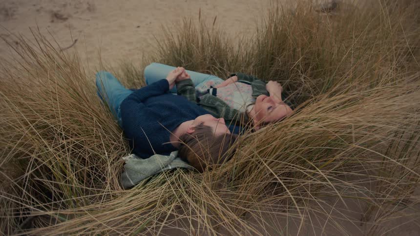 A romantic young couple lies down together in the tall beach grass, sharing a quiet and intimate moment