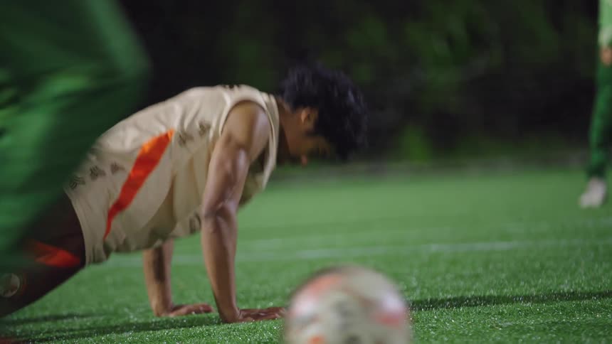 A determined soccer team does push-ups in unison on a turf field during a strenuous night training session