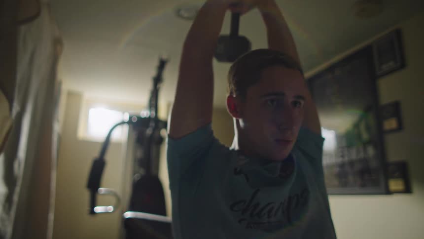 A determined young man smiles with satisfaction while doing overhead tricep extensions in his home gym