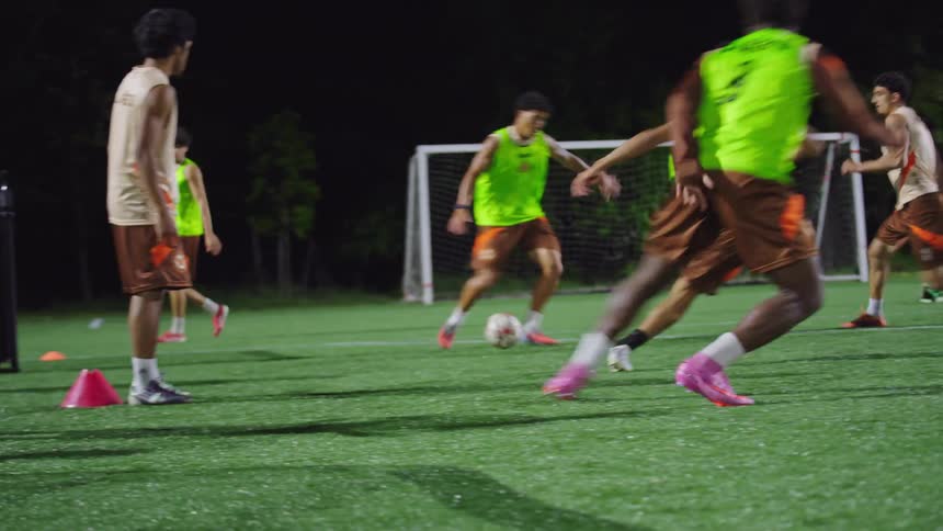 Dynamic low-angle slow-motion shot of soccer players running drills and practicing their dribbling skills on a turf field at night