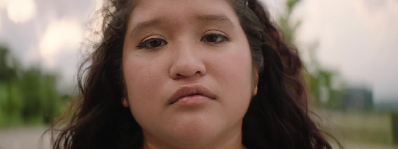 A slow push-in shot comes into focus on the serious face of a young Indigenous woman looking directly at the camera