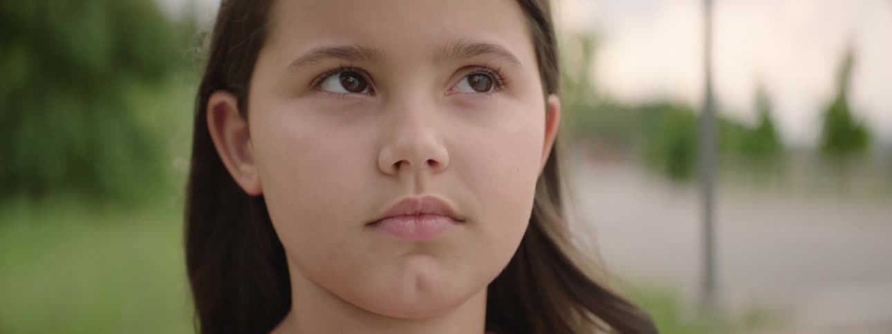 Rack focus close-up reveals the serious and contemplative face of a young girl standing outdoors