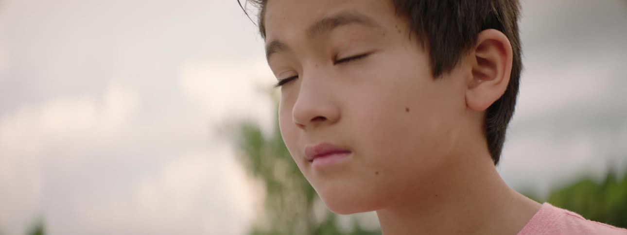 A thoughtful young boy looks up at a faint rainbow in the cloudy sky as the camera slowly comes into focus