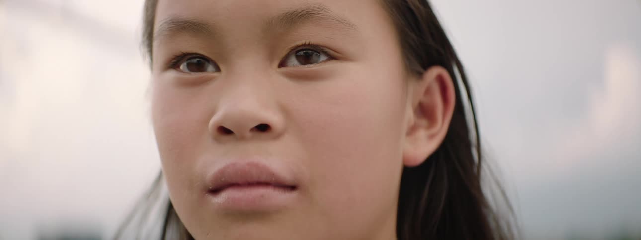 A slow-motion close-up of a young Asian girl's face comes into focus as she gazes thoughtfully into the distance