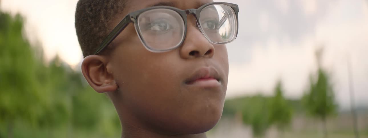 An out-of-focus shot of a young boy with glasses slowly sharpens to a clear, pensive close-up