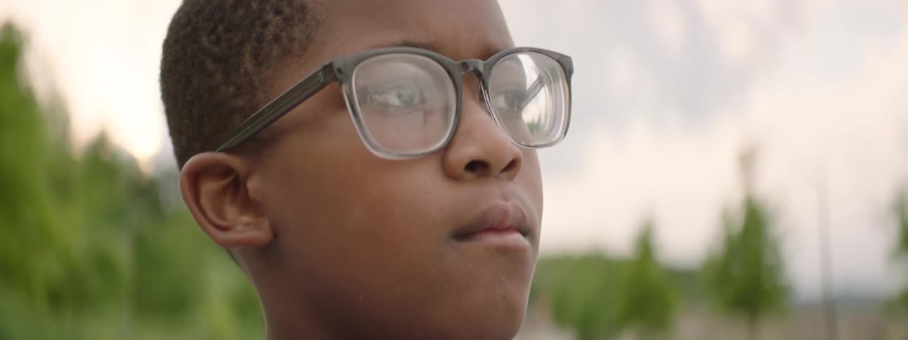 An inspirational close-up shot of a young Black boy with glasses looking thoughtfully and with determination into the distance