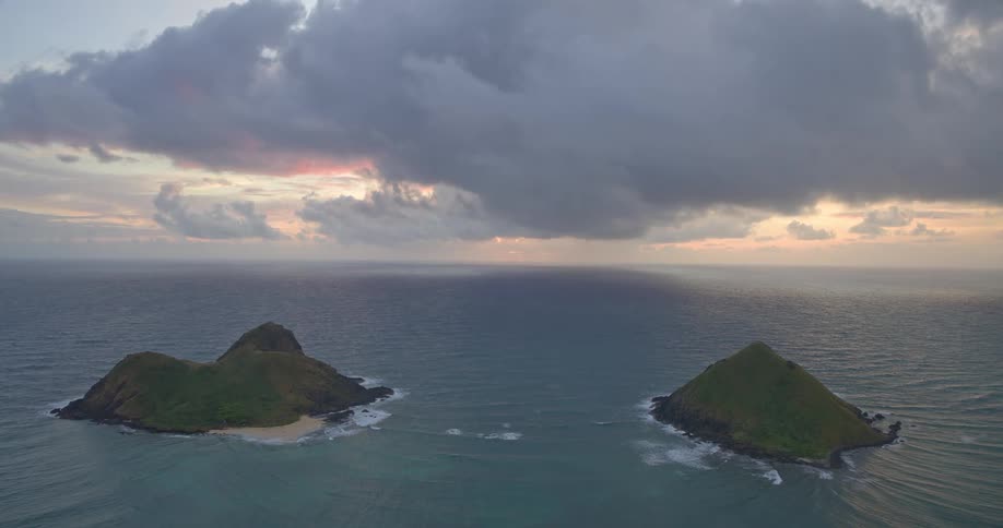 Two lush green islands sit peacefully in the vast ocean under a dramatic cloudy sky during sunrise