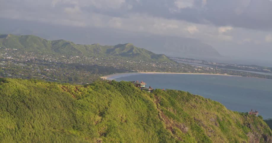 A breathtaking vertical shot pulls back to reveal the stunning view of Kailua, Hawaii, from a lush green mountain ridge at sunrise