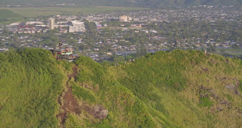 Ascending aerial view of hikers on the green Kaiwa Ridge Trail (Lanikai Pillbox Hike) with panoramic views of Kailua town in the background