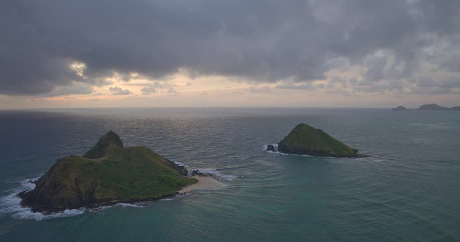 A slow aerial shot reveals the iconic Mokulua Islands off the coast of Hawaii during a moody sunrise