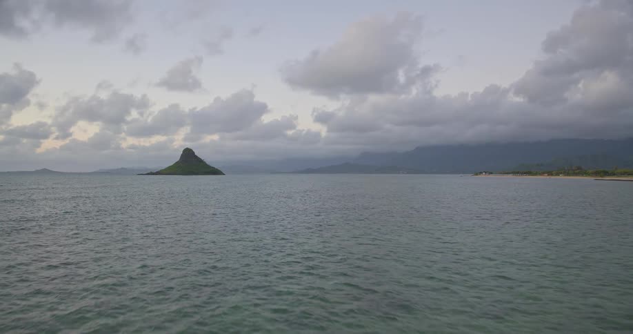 A tranquil and scenic view of Hawaii's Chinaman's Hat island across the calm sea under a cloudy, overcast sky
