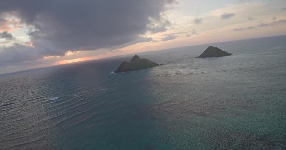 A breathtaking wide aerial view of the Mokulua Islands in the vast ocean during a cloudy and dramatic sunrise in Hawaii