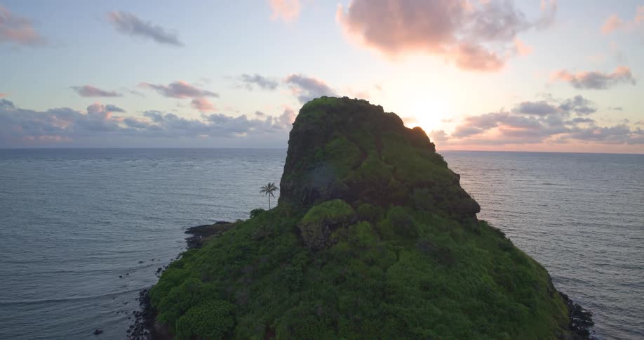 A beautiful aerial shot captures the sunrise over a lush green tropical island sitting in the calm ocean