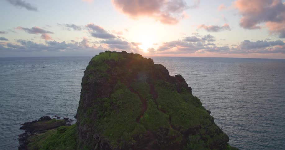 An epic aerial pullback reveals a lush green island in the middle of the ocean during a beautiful sunrise