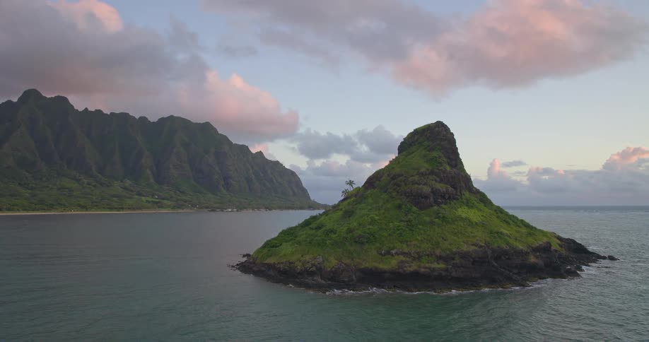 A stunning aerial view reveals a lush green island set against a majestic mountain range during a peaceful sunrise