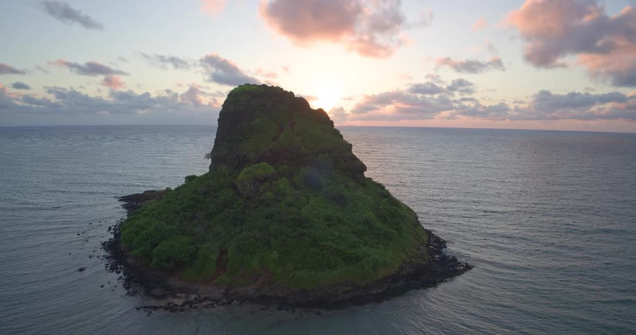 A majestic aerial view slowly pushes in on a solitary lush green island in the ocean at sunrise