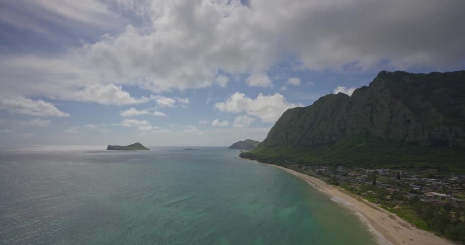 An epic wide shot reveals a stunning tropical coastline where lush green mountains meet the turquoise ocean under a partly cloudy sky