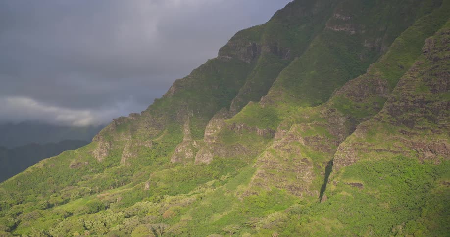 Dramatic light and shadows play across the lush, green slopes of a tropical mountain range