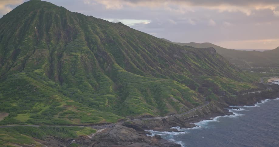 A stunning view of the rugged, green mountainside of Koko Crater meeting the rocky Pacific coastline on Oahu at sunset
