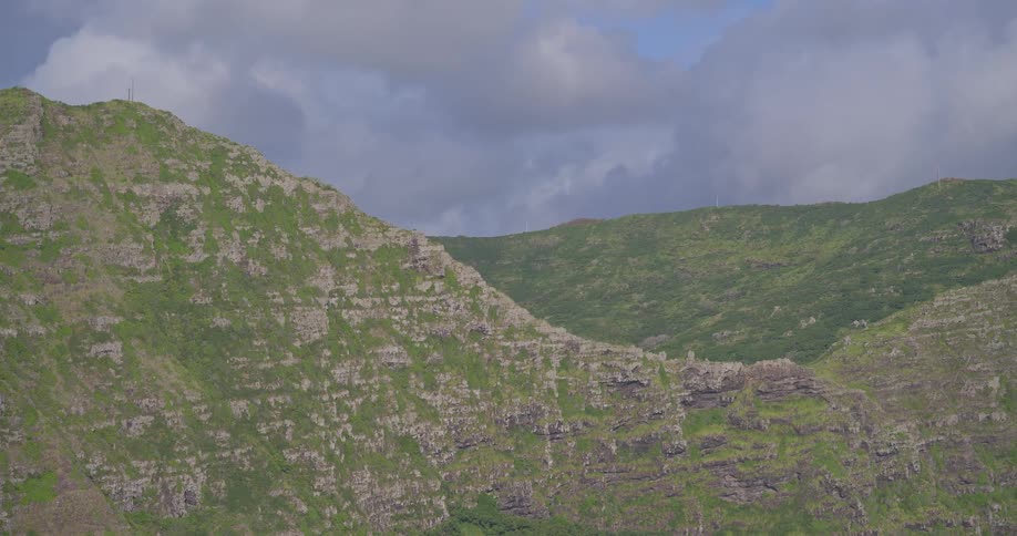 A slow zoom reveals the lush green and rocky details of a majestic mountain range under a cloudy sky