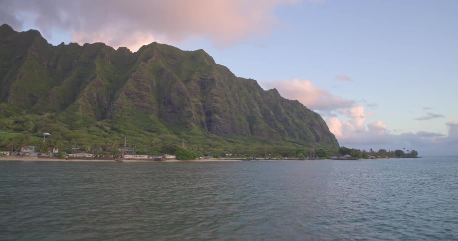 A majestic aerial view of the lush Koolau Mountain Range towering over the tranquil coastline of Oahu at sunrise