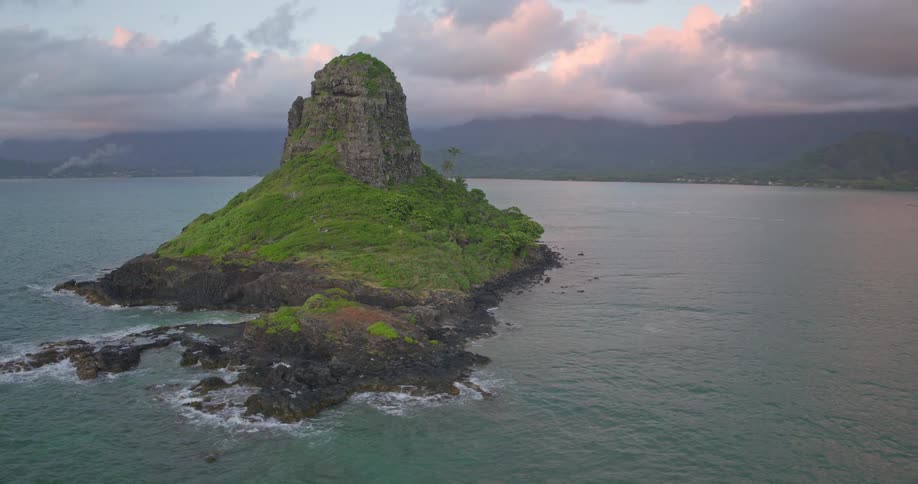 A majestic aerial orbit of the iconic Mokolii island, also known as Chinaman's Hat, reveals the stunning Koolau Mountains of Oahu at sunset