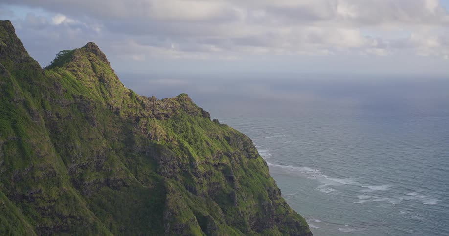 A slow aerial reveal of the stunning, rugged green cliffs of a tropical coastline meeting the vast ocean