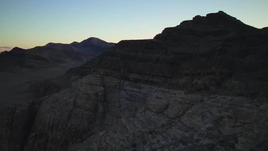 An aerial view of a rugged mountain landscape silhouetted against the sky at dawn
