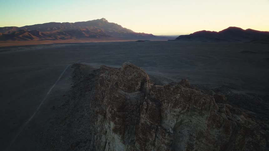 A slow aerial push-in shot over a rugged desert landscape with mountains in the distance at sunrise
