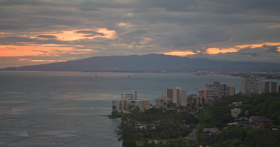 An aerial view of a tropical coastal city with hotels overlooking the ocean during a vibrant sunset