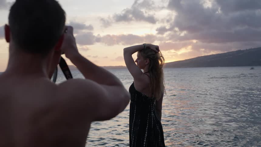A photographer takes a picture of a blonde woman posing in the water at sunset