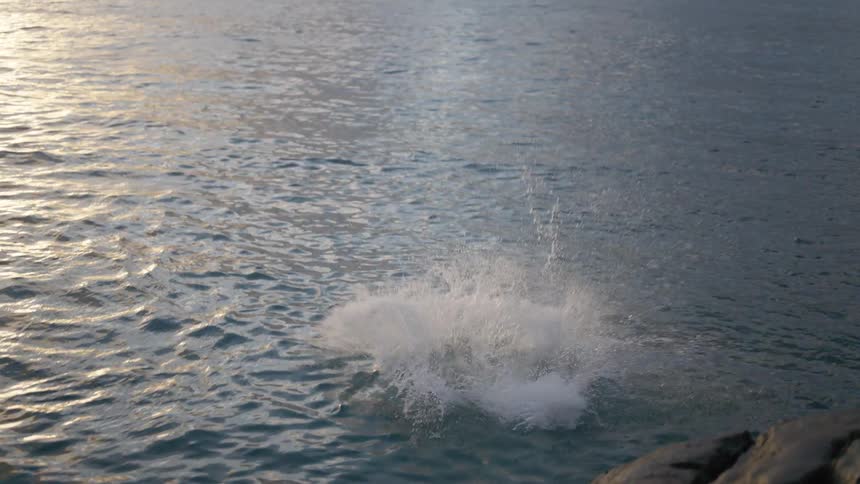 An adventurous man takes a running leap off a rocky cliff into the ocean in dramatic slow motion
