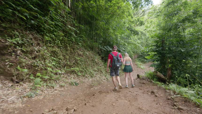 Slow motion footage shows a young man and woman hiking on a muddy trail through a lush, green tropical jungle