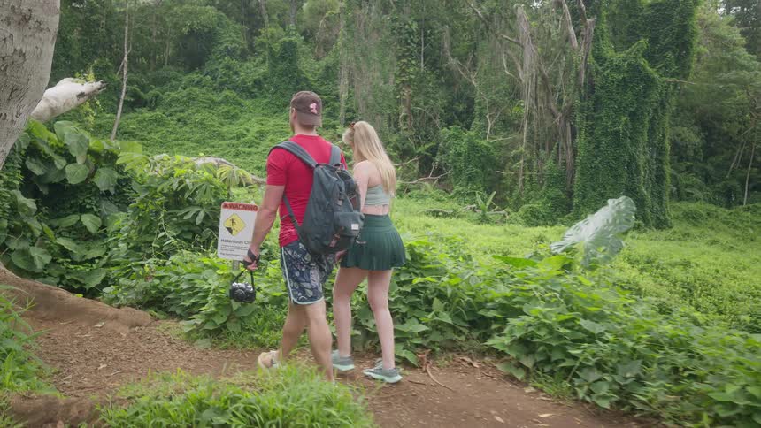 A young couple holds hands while walking along a scenic jungle trail in slow motion