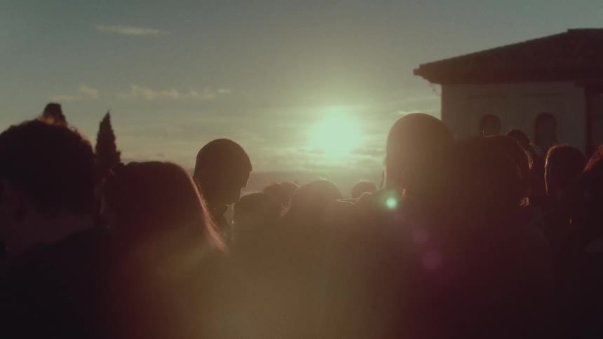 A silhouetted crowd of people gathers to watch the golden hour sunset from a scenic overlook