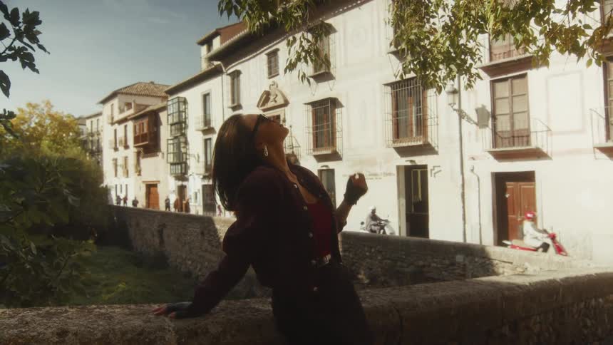 Slow zoom out on a fashionable woman in sunglasses relaxing and enjoying the sun on a stone bridge in a historic European city
