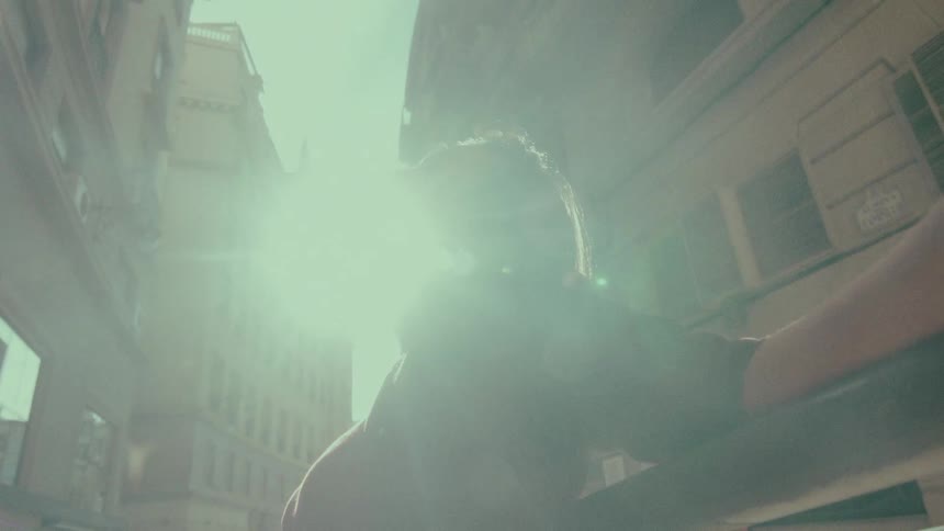 A stylish woman basks in the sun on a European city street, smiling as a bright lens flare washes over the scene