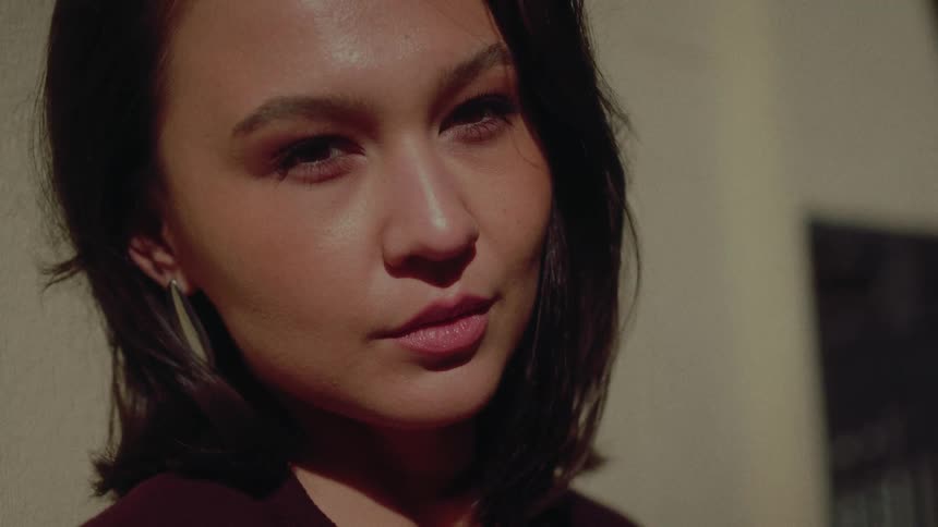 A close-up slow-motion portrait of a beautiful woman basking in warm, dramatic sunlight, turning to look directly at the camera