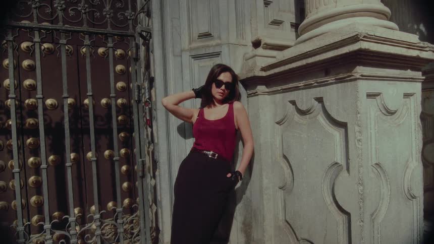 A stylish woman poses in slow motion against an old architectural building on a sunny day