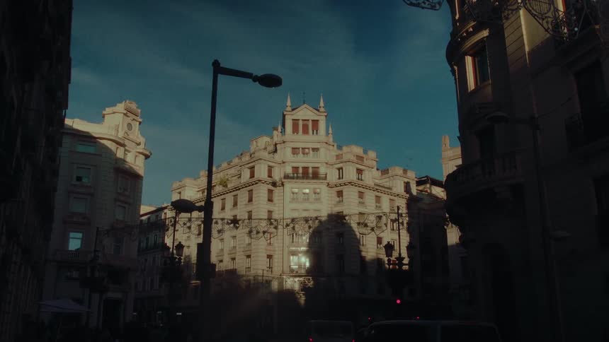 A cinematic view of an ornate European building with contrasting light and shadow during sunset
