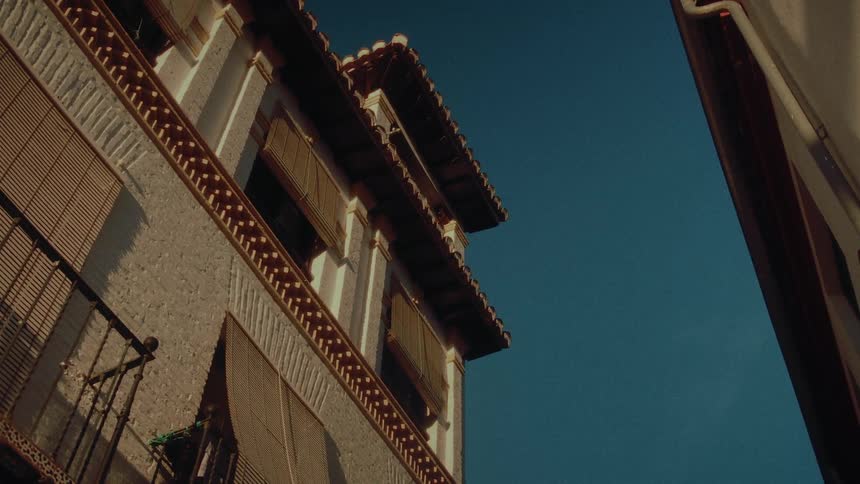 Golden afternoon sunlight hits the side of a traditional Spanish building with balconies and shutters against a clear blue sky