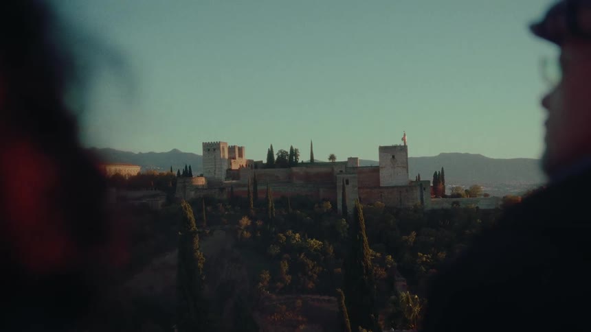A tranquil over-the-shoulder shot of two people admiring the historic Alhambra palace at sunset in Granada, Spain