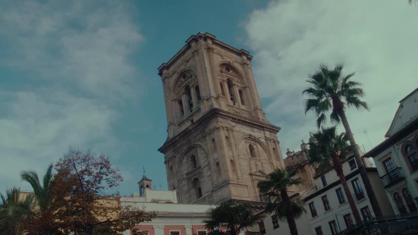 The historic bell tower of the Granada Cathedral stands tall against a cloudy blue sky in Spain