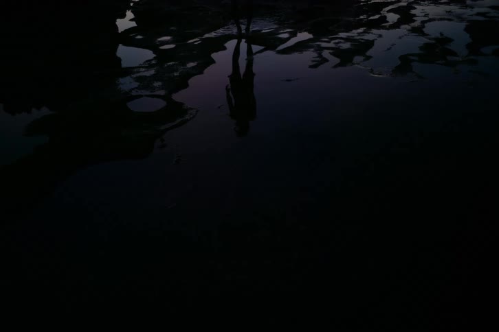 The dark silhouette of a mysterious figure is reflected in a still pool of water at twilight