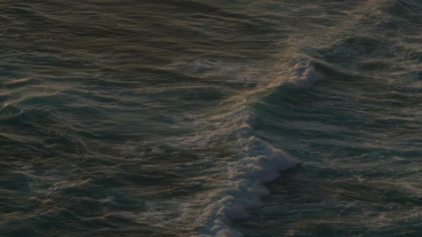 Slow-motion top-down aerial shot of dark ocean waves rolling and churning with sea foam