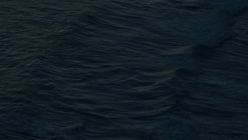 A top-down view of the deep, dark ocean surface as waves move in slow motion