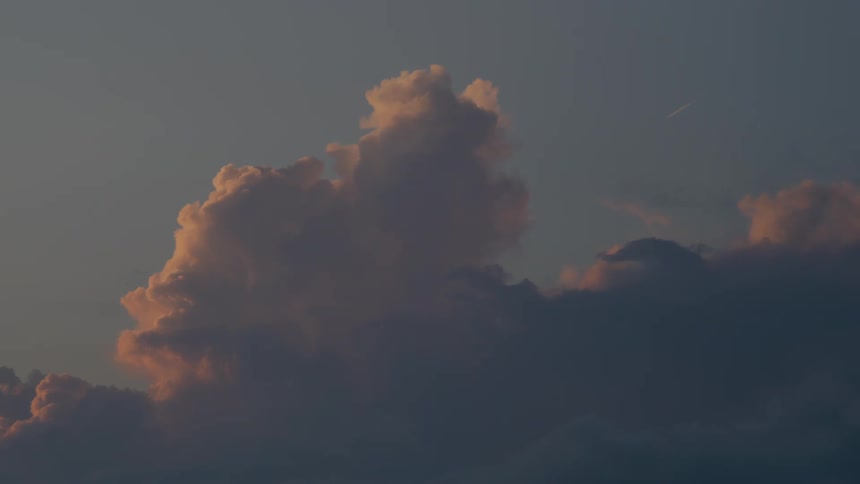 An airplane leaves a trail across the serene sky above fluffy clouds illuminated by the warm light of sunset