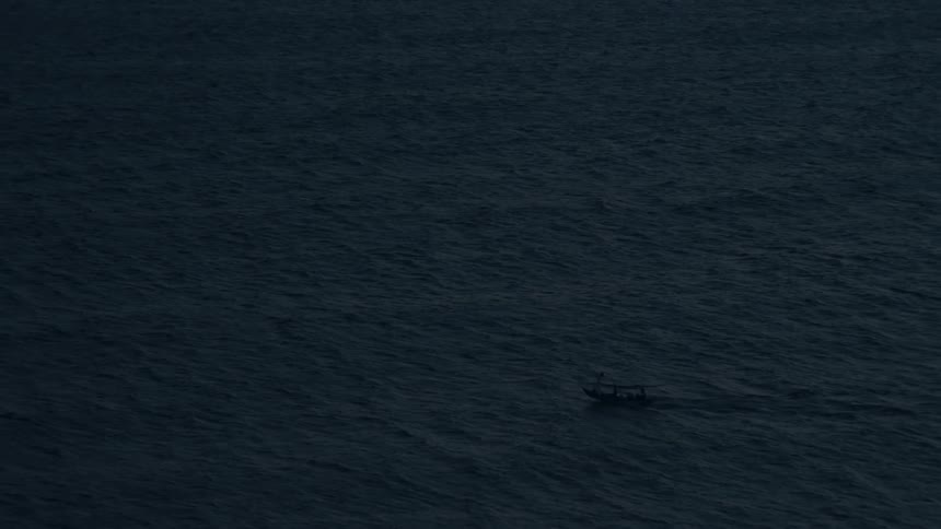 A solitary fishing boat sails across the vast, dark ocean waters at dusk