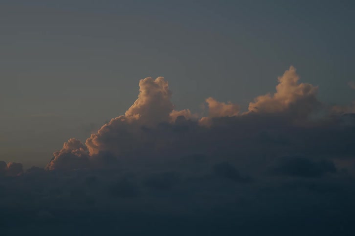 Golden hour light illuminates the tops of fluffy clouds against a serene evening sky
