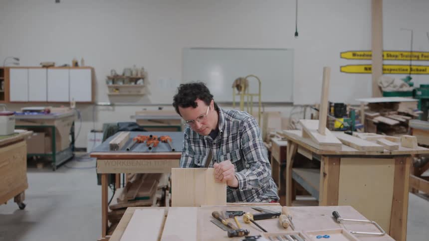 A skilled woodworker carefully saws a joint by hand at his workbench in a spacious workshop